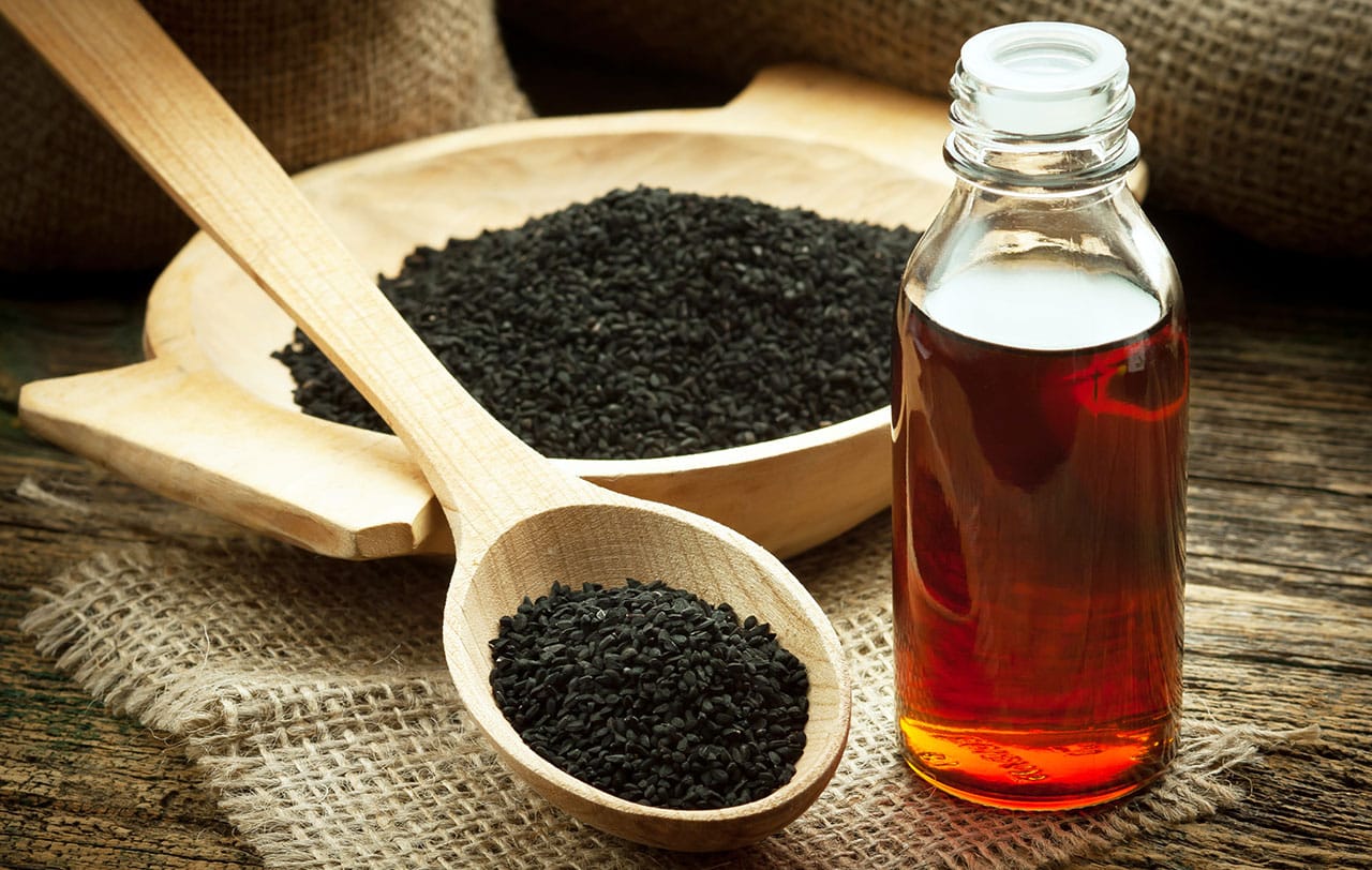 Flasche mit Schwarzkümmelöl neben einer Holzschale und einem Holzlöffel auf einem Tisch