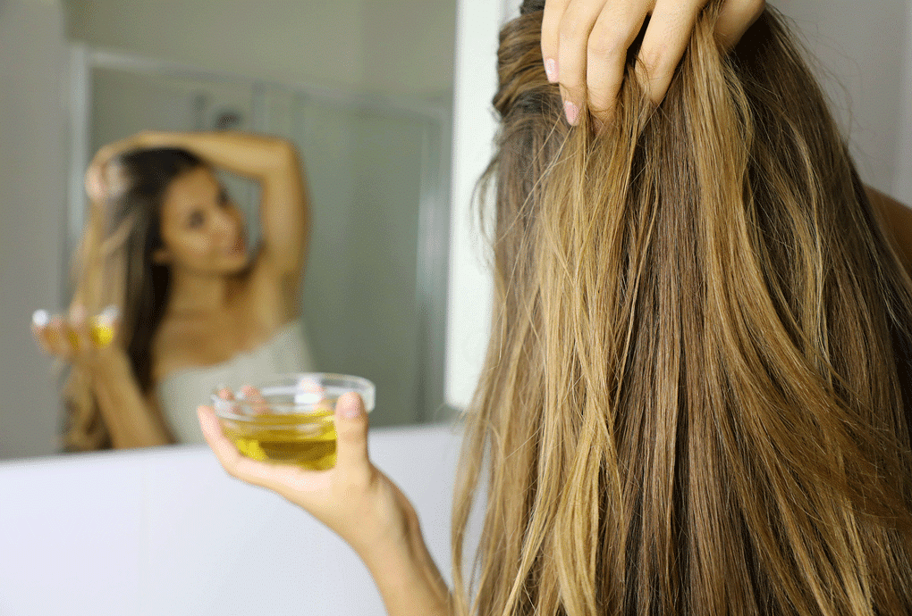Junge Frau vor einem Spiegel massiert nach dem Duschen Öl in ihre Haare