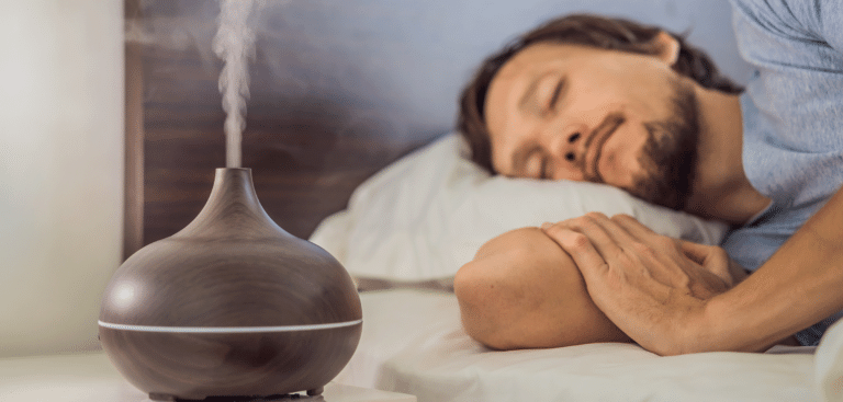 Junger Mann schläft in einem Bett, neben ihm sprüht ein Diffuser