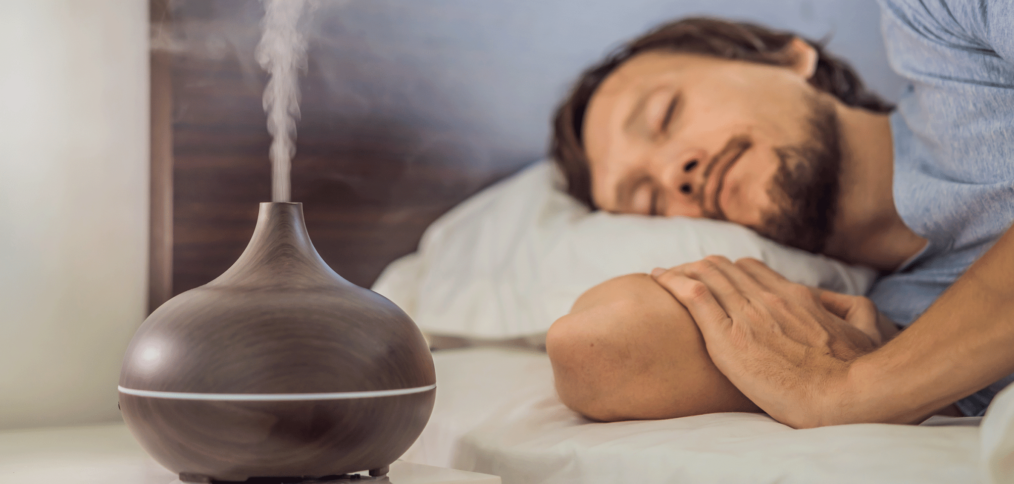 Junger Mann schläft in einem Bett, neben ihm sprüht ein Diffuser