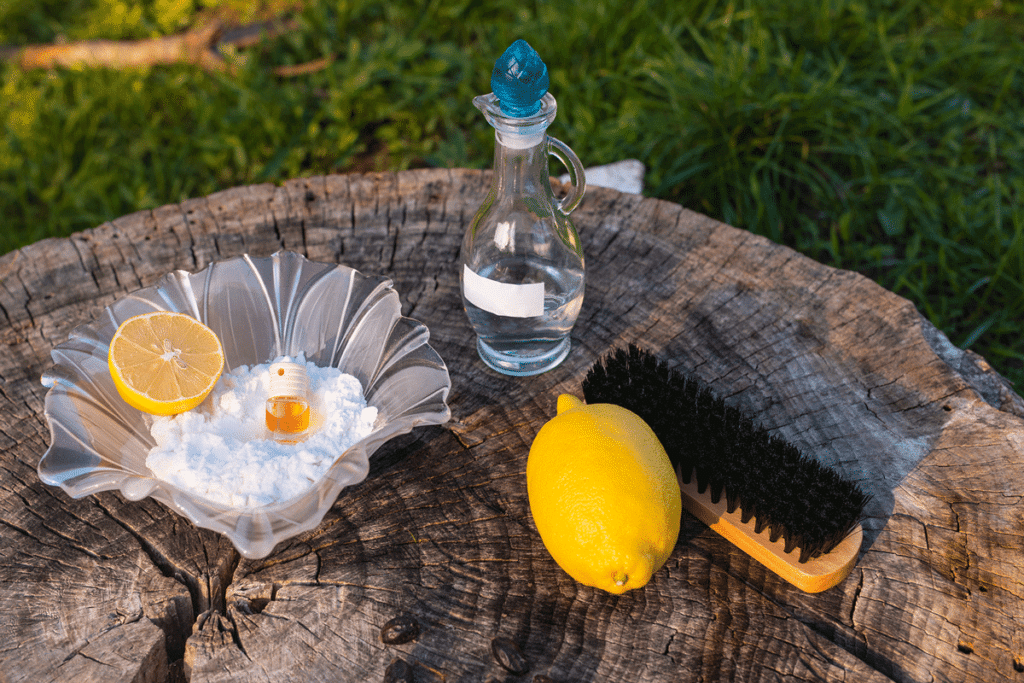 Zitrone, Waschsoda, eine Bürste und ein Fläschchen ätherisches Öl auf einer Unterlage aus Holz