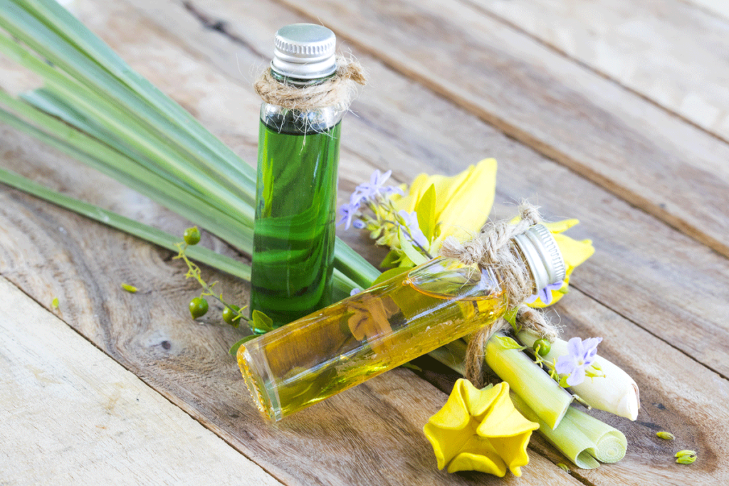 Fläschchen mit Öl neben Ylang Ylang Blüten und Lemongrass auf einem Tisch