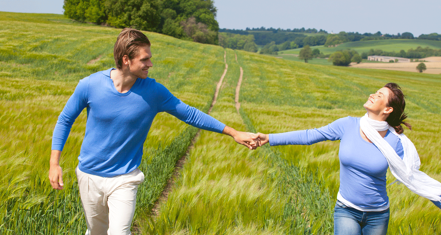 Pärchen läuft Hand in Hand ber eine Wiese