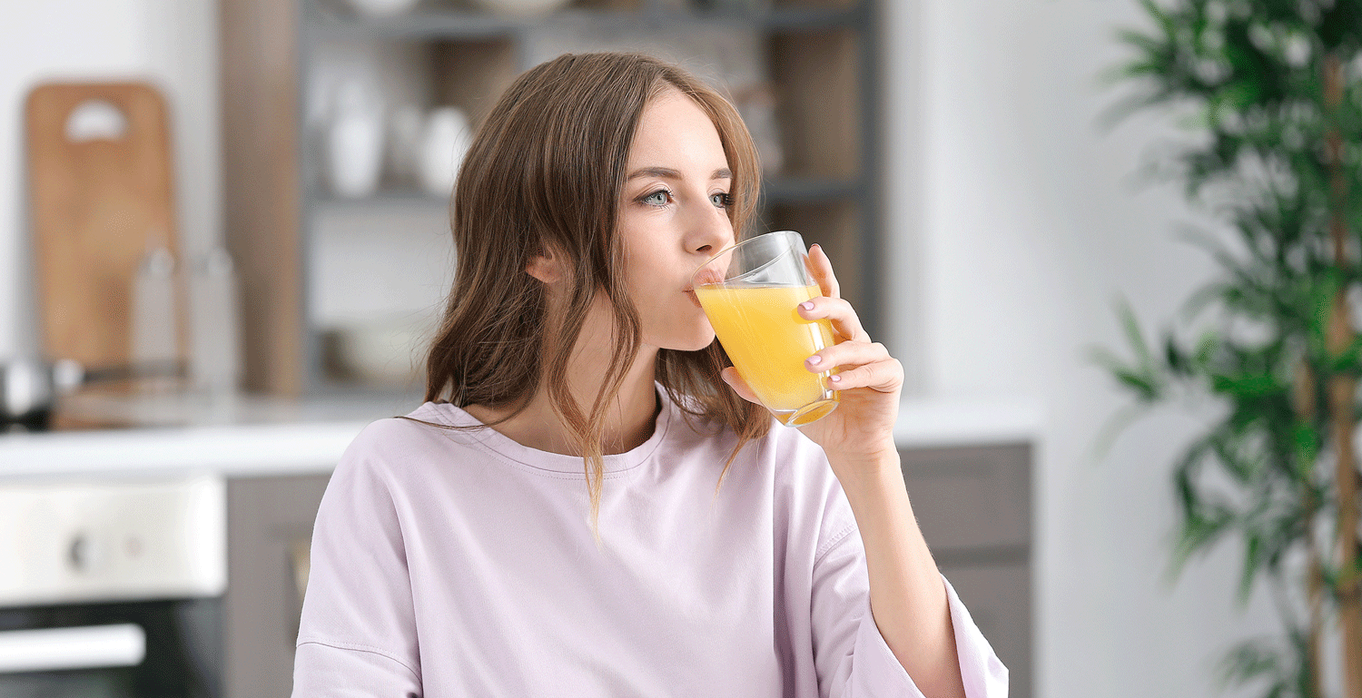 Junge Frau trinkt ein Glas mit Multivitaminbrause