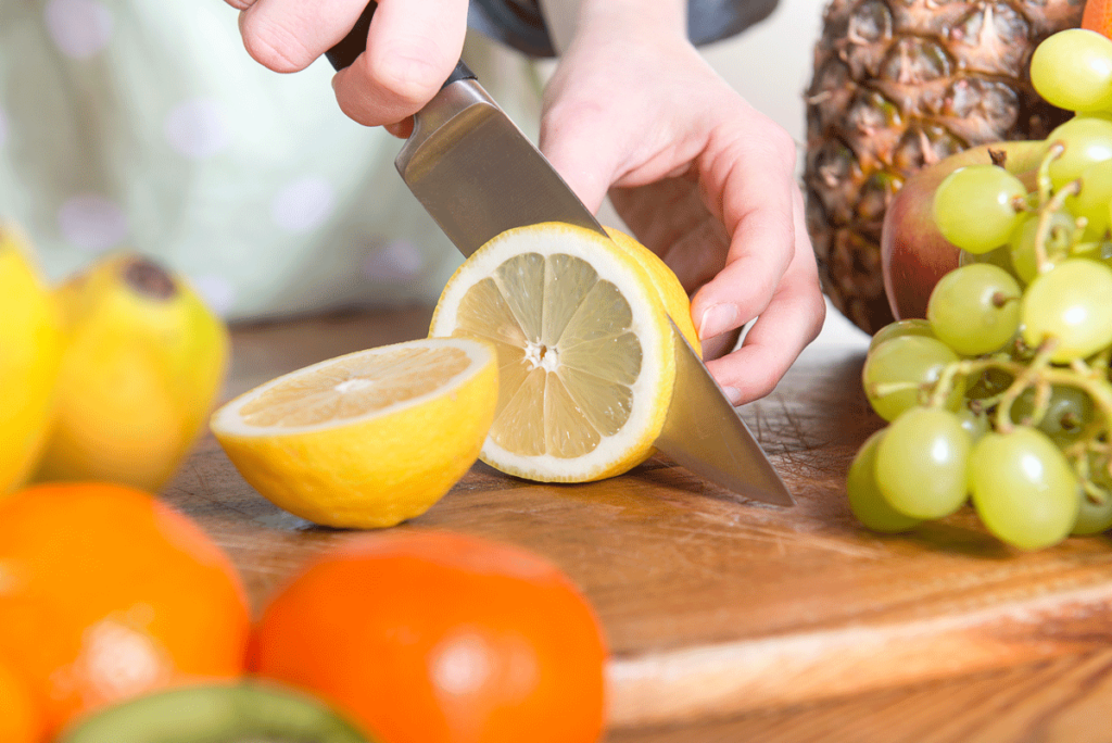 Frische Zitrone wird auf einem Brett aufgeschnitten daneben Weintrauben und Orangen