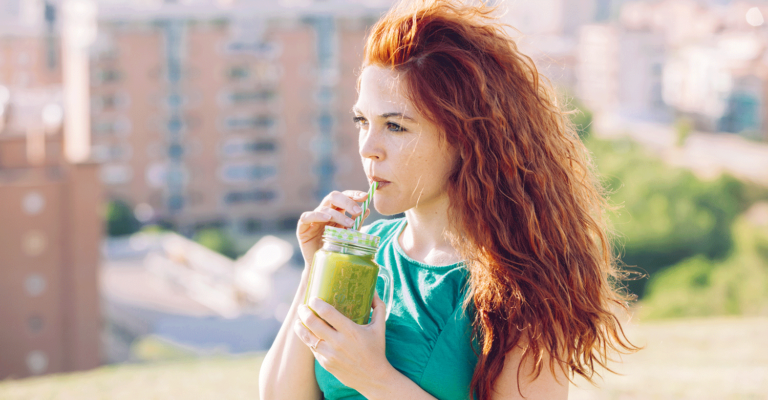 Junge rothaarige Frau trinken einen Smoothie aus einem Glas mit Strohhalm