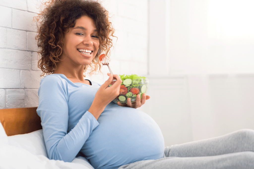 Schwangere Frau sitzt im Bett und isst einen grünen Salat