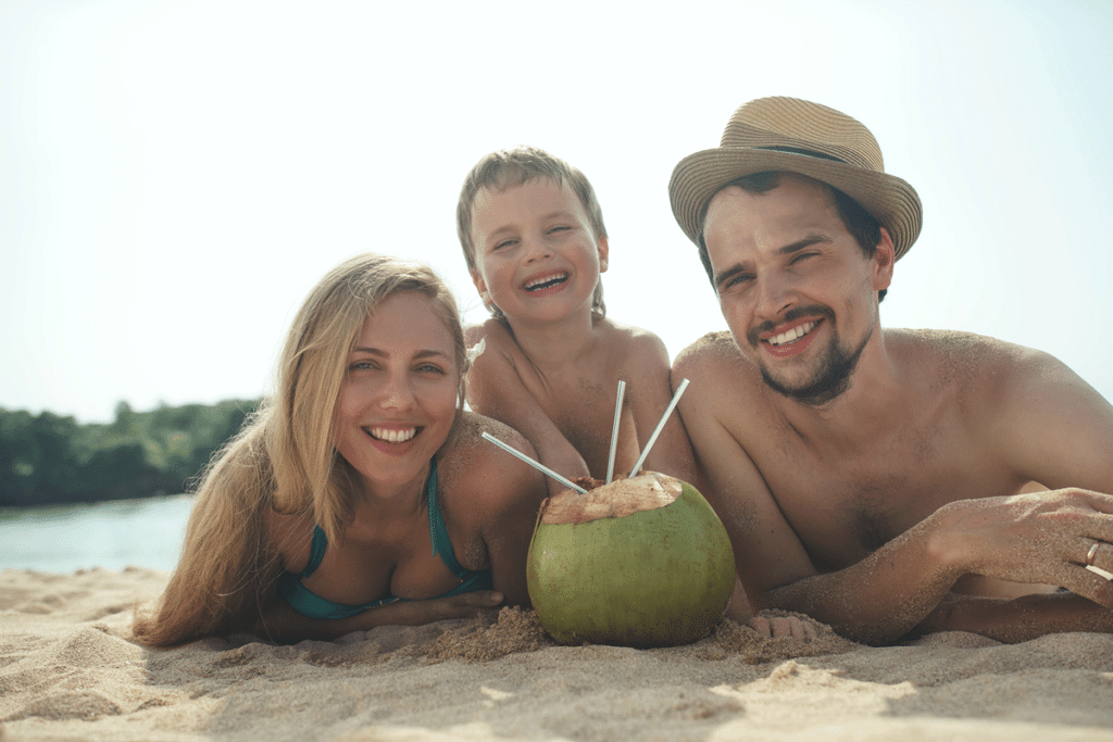 Familie liegt am Strand und trinkt aus einer Kokosnnuss