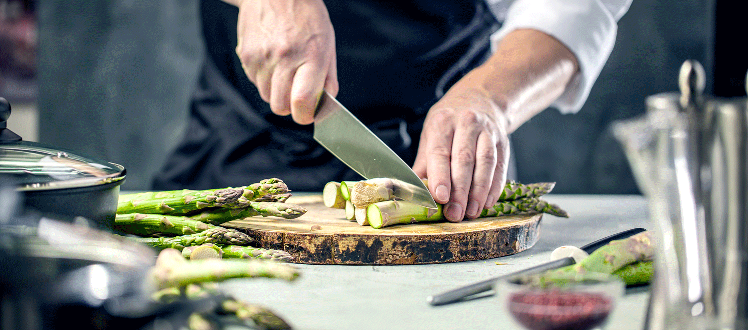 Koch schneidet Spargel auf einem Brett