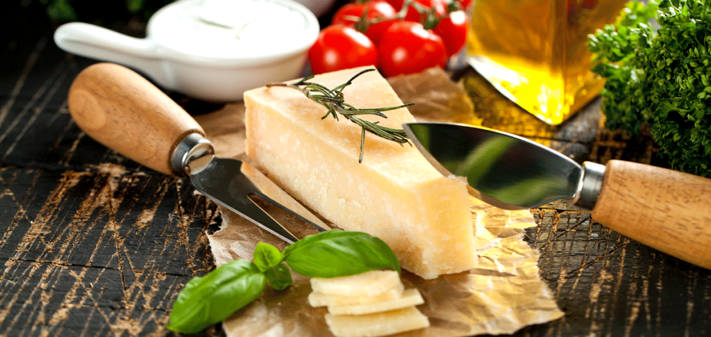 Ein Stück Parmesan mit Basilikum und Tomaten auf einem Brett